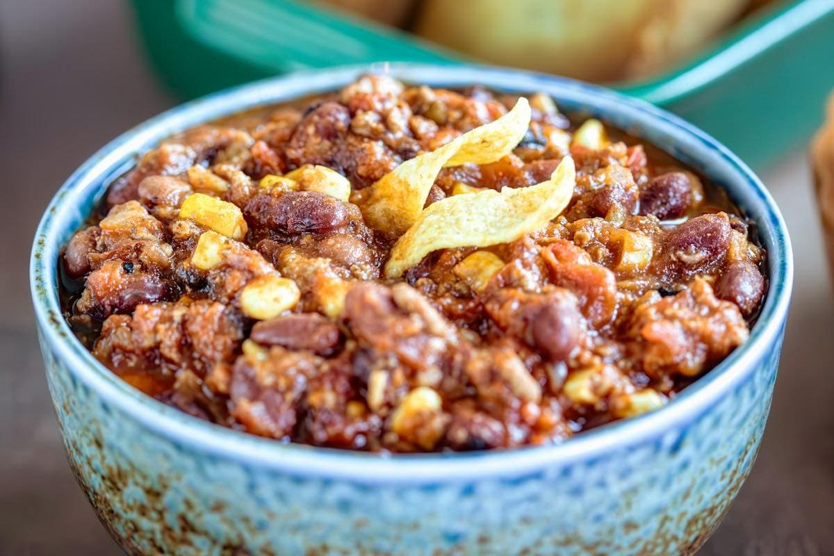 A bowl of chili next to cornbread muffins