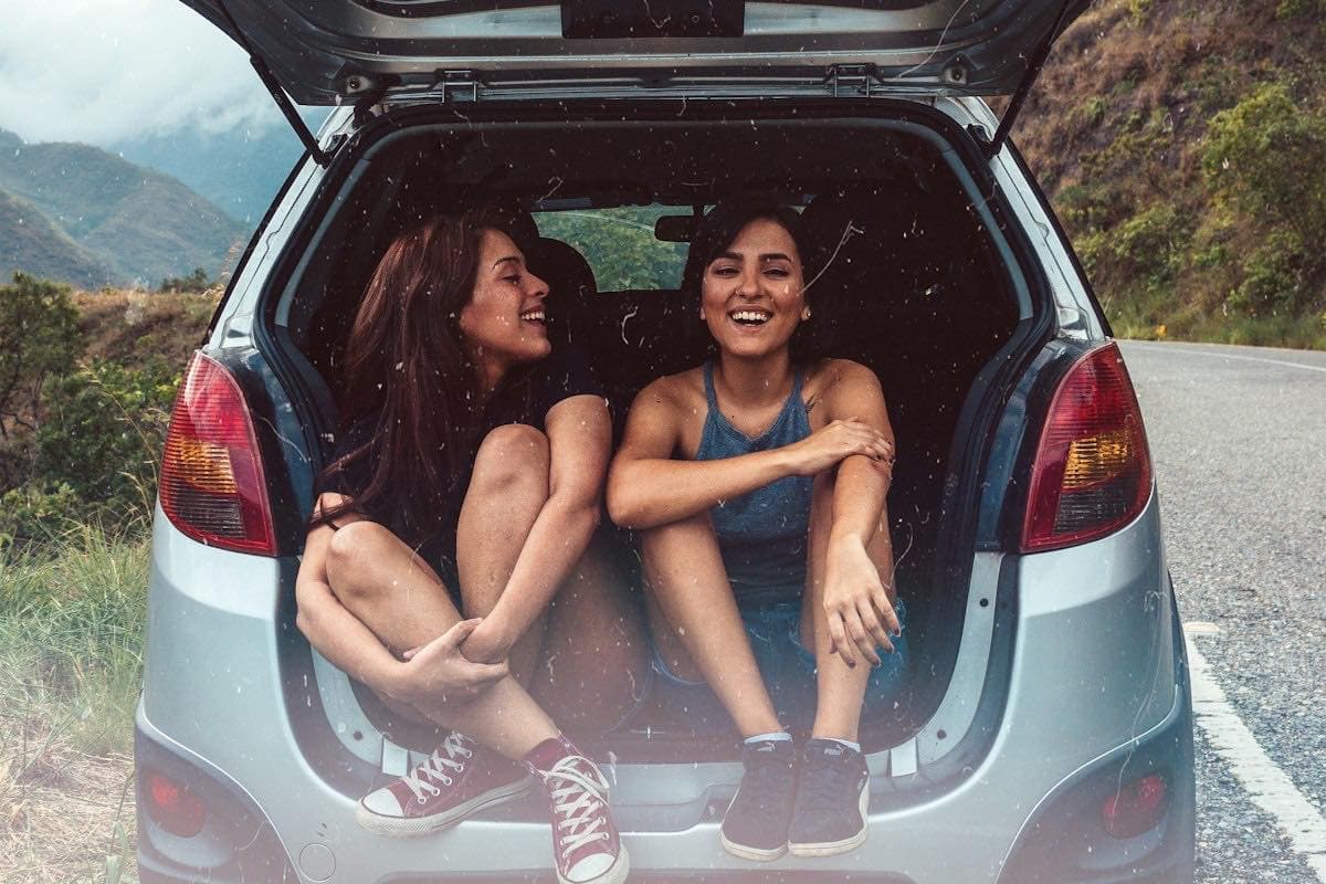 Two friends sitting in the back of a hatchback on a road trip