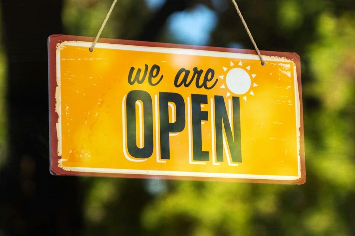 A yellow we-are-open sign hanging in a shop window