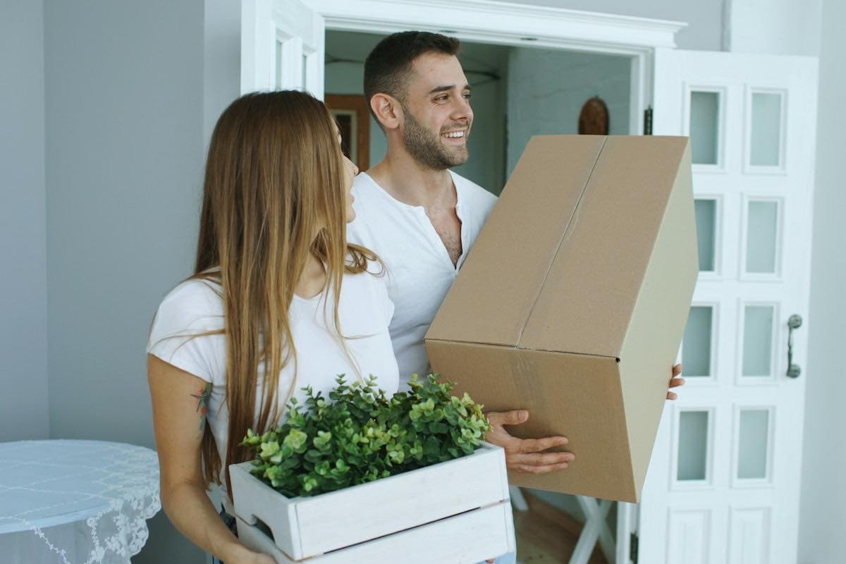 A couple carrying moving boxes into a new home